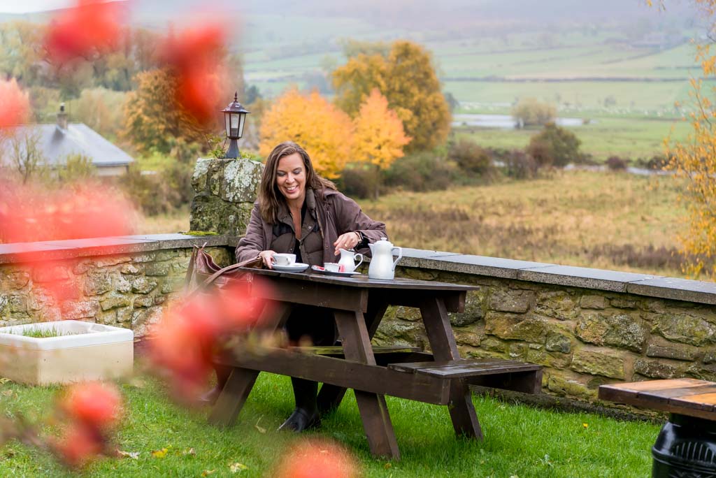 Brand photographer Edinburgh Scotland | woman sitting outdoors at picnic table drinking coffee amongst autumn leaves