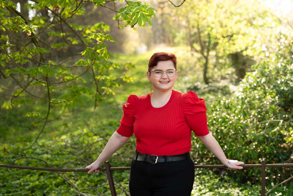 Brand photographer Edinburgh Scotland | woman with short auburn hair wearing bright red top standing in summer woods